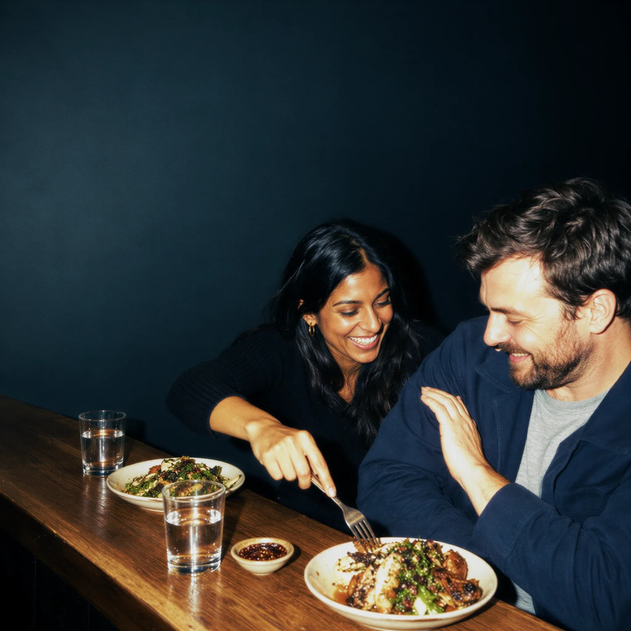 Two people laughing over dinner at a small restaurant at night